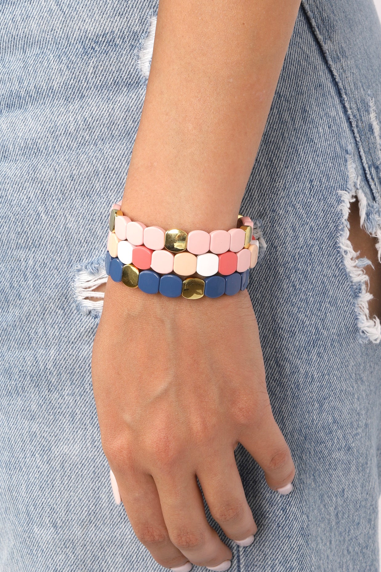 3-piece stretchy bracelet set on wrist of model. Gold beads are shiny, pink and blue beads are smooth in appearance.
