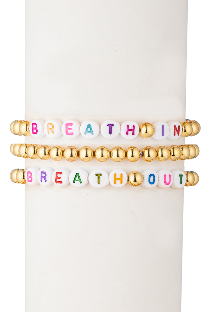 3 piece gold beaded bracelet set. One bracelet reads "breathe in" and one bracelet reads "breathe out" with additional gold beads. Third bracelet is fully gold beaded.