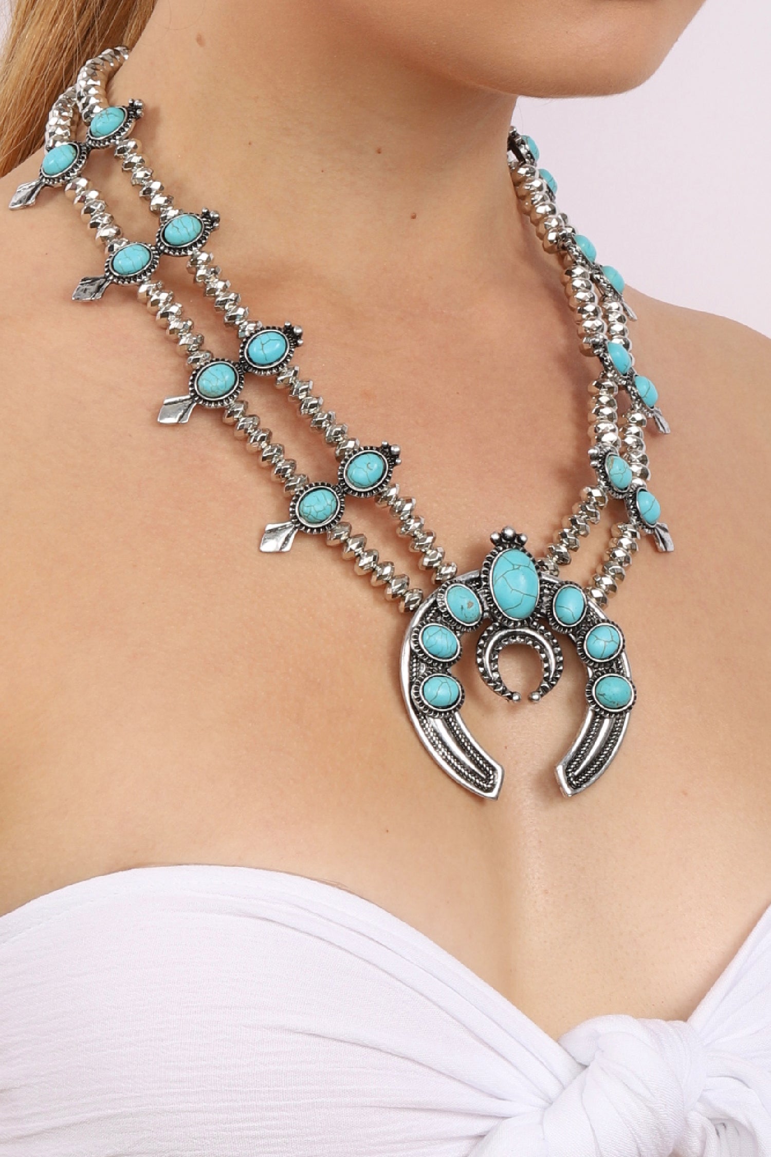 Large silver statement necklace with thick double chain necklace. Necklace is decorated with small circular turquoise stones. Downturned crescent moon shaped pendant hangs with 5 turquoise stones arranged on top half of pendant.