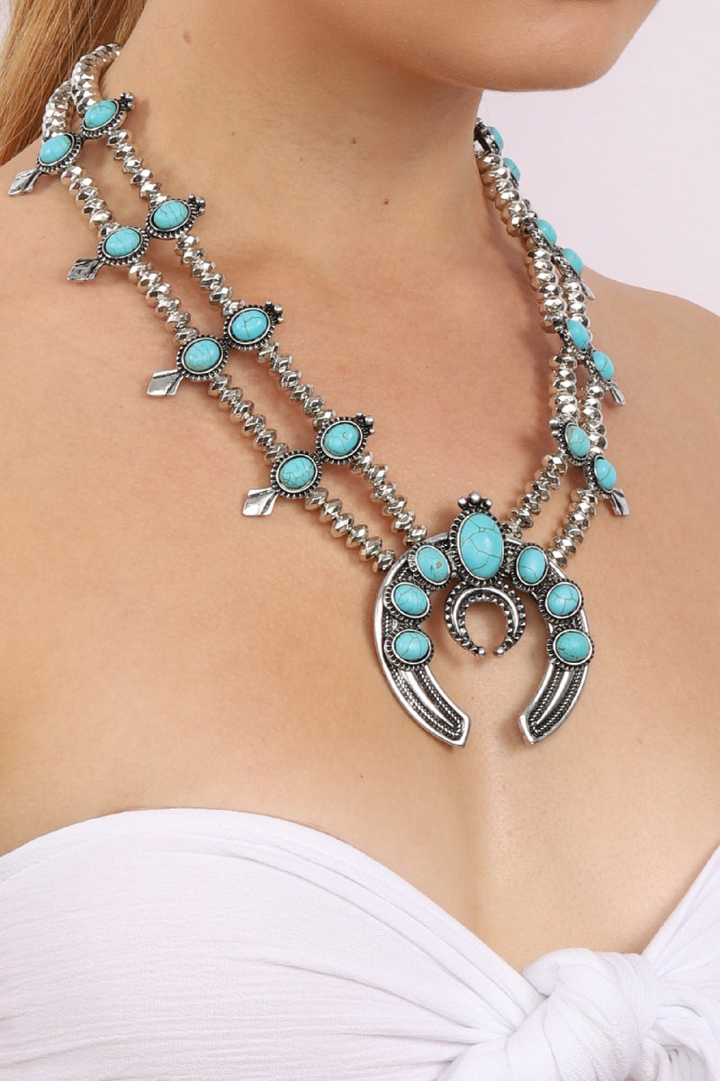 Large silver statement necklace with thick double chain necklace. Necklace is decorated with small circular turquoise stones. Downturned crescent moon shaped pendant hangs with 5 turquoise stones arranged on top half of pendant.